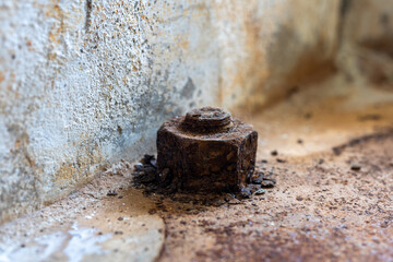 A close-up of a large rusted bolt anchored into a concrete surface, surrounded by corrosion flakes...