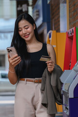 Young business woman using smartphone and credit card next to ATM