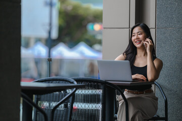 Businesswoman working remotely using laptop and talking on phone in cafe