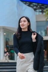 Young businesswoman walking in the city holding jacket and looking away