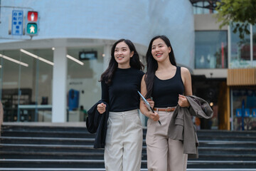 Two young businesswomen walking and talking on city street