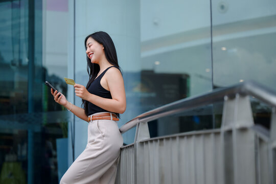 Young business woman using smartphone and credit card for online shopping near office building