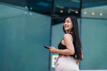 Smiling businesswoman holding smartphone turning around near office building