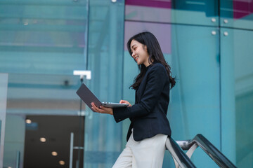 Young businesswoman working on laptop outside modern office building
