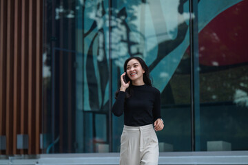 Smiling businesswoman walking and talking on cell phone outside modern office building
