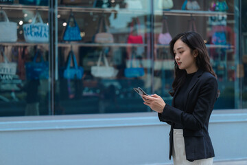 Businesswoman using smartphone while walking past fashion store window