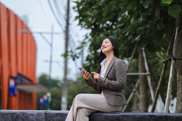 Obraz premium Asian businesswoman is using mobile phone and relaxing outdoor during break time
