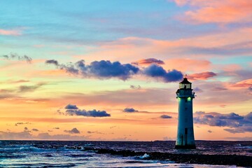 Lighthouse at dusk with dramatic clouds and unset over ocean