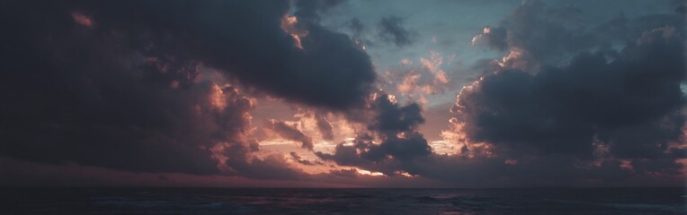 Dramatic sky over the ocean, with sunset colours breaking through heavy dark clouds painting a