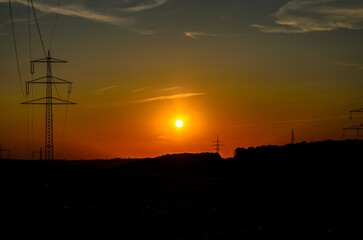 Bright orange sunset in Iserlohn with silhouettes of high-voltage towers and hills on horizon