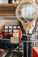 Vintage automotive workshop interior with large industrial spotlight on black stand, retro gauges on brick wall, tires and hoses creating rustic garage atmosphere