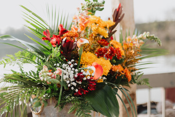 Colorful floral arrangement with red, orange, yellow flowers, lush greenery, and rustic metal...