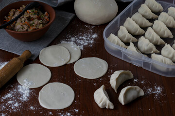 Raw dough rounds on wooden table with flour and rolling pin before filling for homemade pork gyoza preparation process traditional Japanese dumplings making step kitchen view food concept