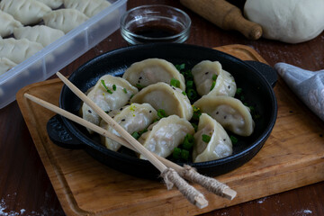 Pan fried Japanese pork gyoza served on black plate with dipping sauce on wooden tray garnished...