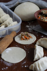 Rolling and filling pork gyoza dumplings at home on wooden surface with flour dough circles and visible ingredients traditional Japanese preparation process before cooking