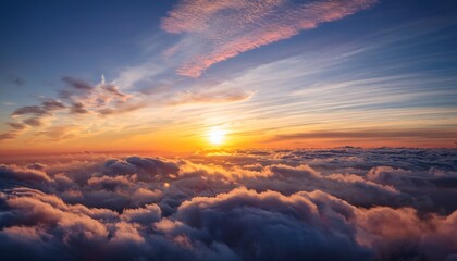 vast expanse of clouds bathed in warm glow of sunrise sunset with sun visible near horizon casting golden light across sky clouds fluffy dense with some closer to viewer appearing tinged in pink