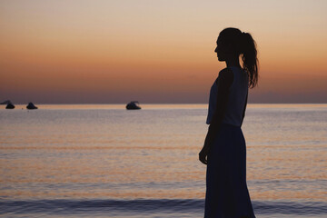 Silhouette of a woman walking along the beach at sunset and enjoying the peaceful sea view....