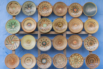 Collection of traditional, handcrafted ceramic plates and bowls displayed against a bright blue wall.  Photo taken in Astra ethographic open air museum in Sibiu, Romania.