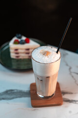 Iced Cappuccino with Thick Milk Foam on Glass. Blurred slice of berry layer cake in background. Ideal for cafes, drink menus, and social content.