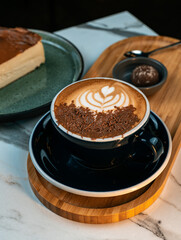 Mocha coffee with chocolate shavings and heart latte art served with truffle and Basque cheesecake on a wooden tray. 