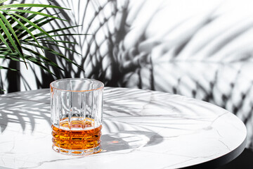 Japanese single malt whiskey served in a glass on a stylish marble table with leaf shadows creating...