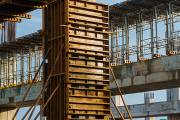 Close-up image of formwork for concrete pillar construction at Saraburi electric train station. Scaffolding, support beams, and framework captured in natural sunlight, showing technical detail of infr