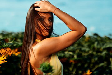 Beautiful young woman posing in sunflower field touching her hair