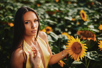 Beautiful woman wearing yellow dress touching sunflower in sunflower field