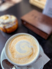 Close-up of a creamy coffee cup with intricate latte art, accompanied by a delicious pastry on a dark wooden table, creating a cozy cafe atmosphere for relaxation