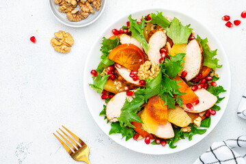 Yummy persimmon salad with grilled chicken, pomegranate, walnuts, oranges and lettuce, top view