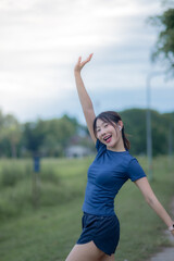 A woman is standing in a park, smiling and waving her arms