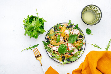 Fresh salad with chicken, orange, raisins, mixed herbs and crunchy seeds, white table background, top view