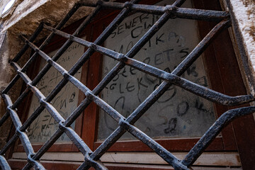 Graffiti-Tagged Window Behind Weathered Metal Grille in Urban Setting