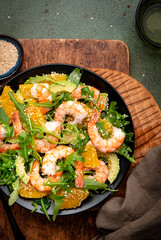 Gourmet seafood salad with shrimps, avocado, orange, arugula and sesame seeds on green stone background. Top view