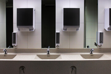 Interior of a modern public restroom with multiple sinks with chrome automatic faucets, mirrors,...