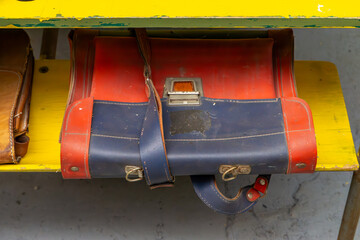 Worn-out red and blue vintage school satchel from the communist era, placed on a yellow tabletop....