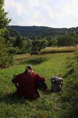 A young guy in a red shirt and jeans with a guitar travels alone through green mountains and nature.