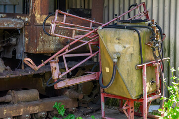 Worn-out field sprayer with a yellow tank and red metal frame, standing next to a rusty...