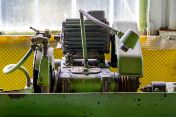 old green industrial machine with an electric motor in a workshop. Visible signs of wear, grease,...