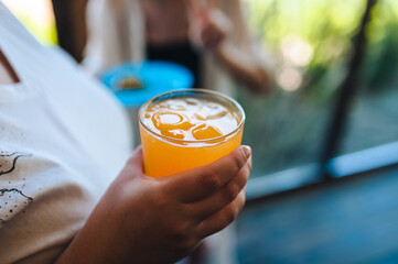 Photo of orange juice, cocktail with ice in hands of woman on summer vacation.