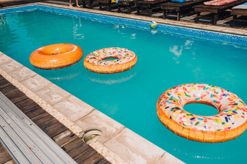 Photo of a large swimming pool with blue water and inflatable accessories, rings, matrices for...
