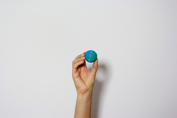 Single hand reaching up holding miniature Earth globe against neutral background, symbolizing environmental aspirations and global responsibility. Planet earth. Earth day concept. Save the planet