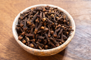 Stone bowl with dried clove buds, used for cooking and traditional medicine, close-up, spices collection