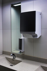 Interior of a modern public restroom with sink, chrome automatic faucet, mirror, soap and towel...