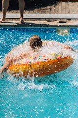 Adult man swimming, having fun, splashing on inflatable ring in pool in summer during leisure time...