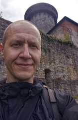 Selfie photo of a forty year old man with the defensive towers of a stone castle behind his back. Traveler selfie. Exploring the sights of the Czech Republic. Traveling during vacation.