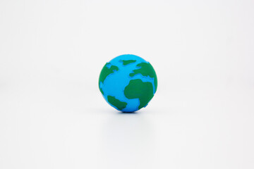 Miniature Earth globe model with blue oceans and green continents sitting alone on clean white surface background. Earth day concept. Environmental conservation. Global unity concept. 