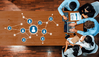 Overview of a business meeting emphasizing networking and data analysis, showcasing diverse professionals collaborating around a table with digital tools and charts. Amity