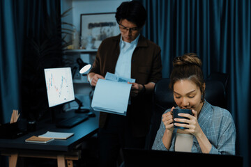 Thinking businesswoman trader drinking coffee while working on pc with coworker looking business...