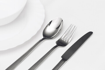 Shiny metal cutlery on white background. Knife, fork and spoon next to clean plates. Elegant dining...